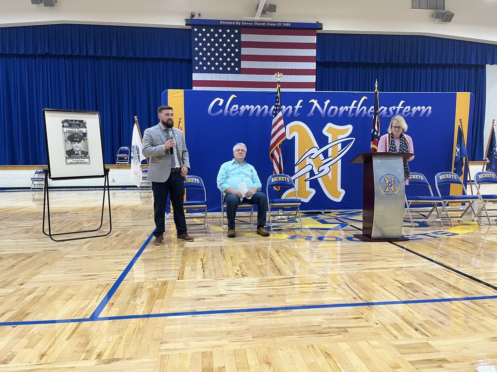 Tyler Kozloski addresses students at Clermont Northeastern High School while Cliff Riley (seated) and social studies teacher Becky Loughran, who emceed the ceremony, look on. (Photo by Dick Maloney.)